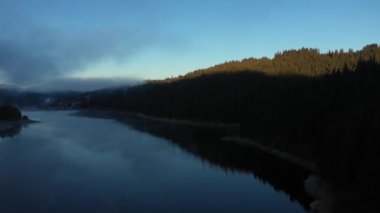 Sabahın erken saatlerinde sisli şafak ışıklarıyla bir gölün üzerinde uçmak. Hava aracı görünümü