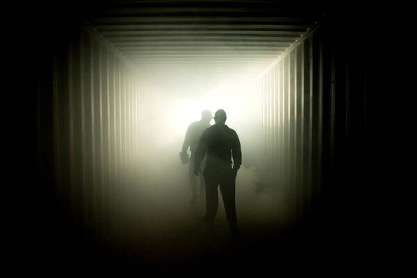 Silhouette of people walking in a dark subway tunnel to the light