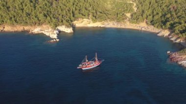 Yunanistan 'ın Thassos adasının kayalık Akdeniz kıyısında yelken açan bir turist gemisinin hava manzarası.