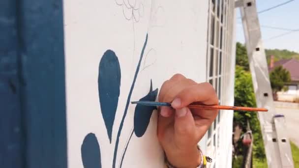 Hand of a girl painting blue flower motif, tulip on a whitewashed wall
