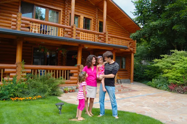 Feliz familia sonriente cerca de la casa de madera — Foto de Stock