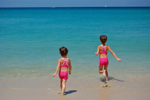 Twee meisjes in pakken zwemmen op tropisch strand — Stockfoto