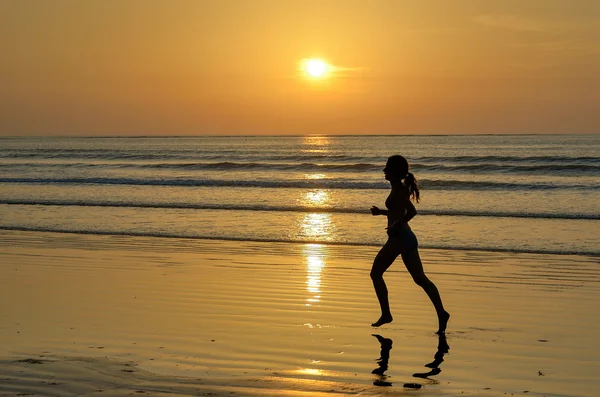 Silueta ženy běžec běží na pláži při západu slunce — Stock fotografie