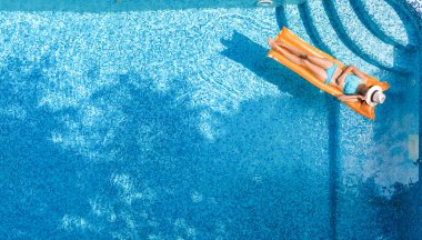 Yüzme havuzunda dinlenen güzel genç bir kadın, şişme yatakta yüzen ve aile tatilinde suda eğlenen bir kız, tropikal tatil beldesi, yukarıdan drone manzarası