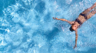 Yüzme havuzundaki aktif genç kız yukarıdan drone görüntüsü, mavi su havuzunda yüzen genç kadın, tatil beldesinde tropikal tatil 