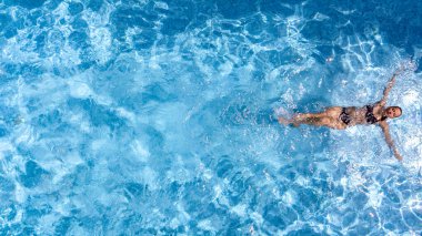 Yüzme havuzundaki aktif genç kız yukarıdan drone görüntüsü, mavi su havuzunda yüzen genç kadın, tatil beldesinde tropikal tatil 