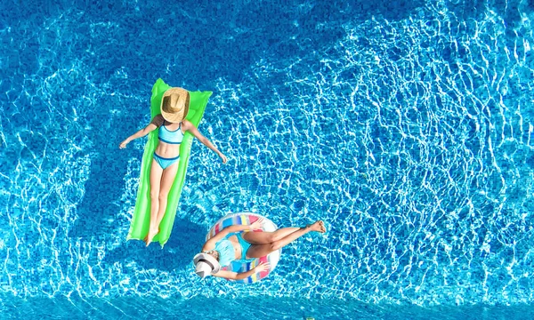 在游泳池里的孩子们从空中俯瞰着天空 快乐的孩子们在充气的环形甜甜圈和床垫上游泳 活跃的女孩们在度假度假时在水里玩得很开心 — 图库照片