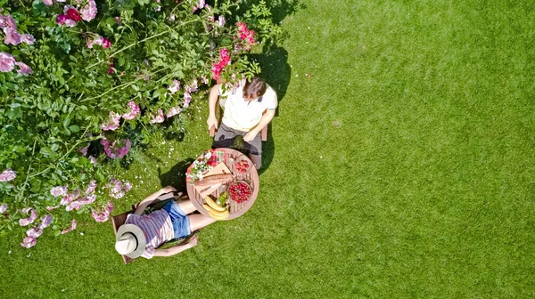 在浪漫的日子里 年轻夫妇在美丽的玫瑰花园里享用着食物和饮料 在空中俯瞰着男人和女人在公园外面一起吃喝的景象 — 图库照片