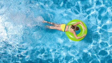 Yüzme havuzundaki aktif genç kız yukarıdan havuz manzaralı, çocuk gevşiyor ve şişme halka donutla yüzüyor ve aile tatilinde suda eğleniyor, tropikal tatil beldesi