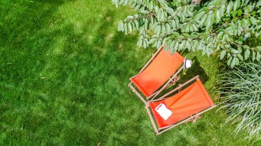Güneş yatağı sandalyeli yaz bahçesi çimenlerin üstünde gökyüzü manzaralı, yeşil park ağaçları ve yukarıdan rahatlamak için bir yer.