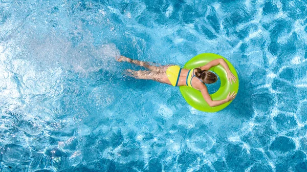 Yüzme havuzundaki aktif genç kız yukarıdan havuz manzaralı, çocuk gevşiyor ve şişme halka donutla yüzüyor ve aile tatilinde suda eğleniyor, tropikal tatil beldesi