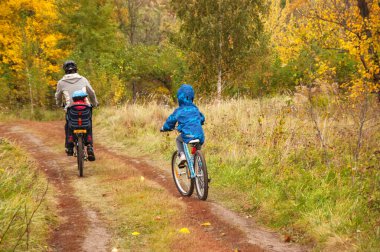 Altın sonbahar parkında aile bisikleti, aktif baba ve çocuklar bisiklet sürüyor, aile sporu ve çocuklarla açık havada spor yapıyor.