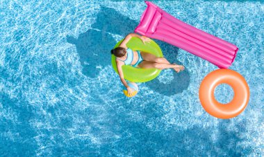 Yüzme havuzundaki aktif genç kız yukarıdan havuz manzaralı, çocuk gevşiyor ve şişme halka donutla yüzüyor ve aile tatilinde suda eğleniyor, tropikal tatil beldesi