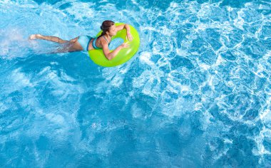 Yüzme havuzundaki aktif genç kız yukarıdan havuz manzaralı, çocuk gevşiyor ve şişme halka donutla yüzüyor ve aile tatilinde suda eğleniyor, tropikal tatil beldesi