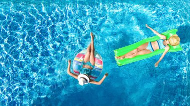 Havuzda yüzen çocuklar yukarıdan insansız hava aracı görüntüsü, mutlu çocuklar şişme halka donut ve şiltede yüzüyor, aktif kızlar tatilde aile tatilinde suda eğleniyor.