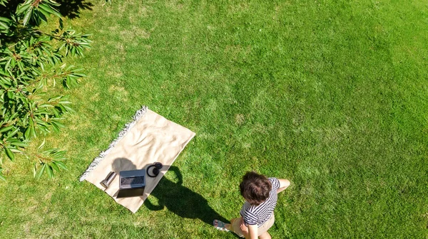公園内のラップトップコンピュータを持つ若い女性 学生の女の子のフリーランス仕事やヘッドフォンやラップトップで芝生の上でオンライン屋外で勉強 上から空中ドローンビュー — ストック写真