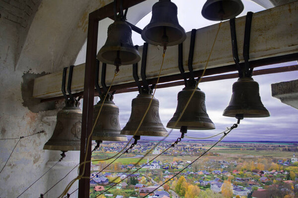 Bells on the old bell tower, Orthodox monastery. Far away, there is a rural landscape, fields, trees, houses. Religion, traditional Russian culture.
