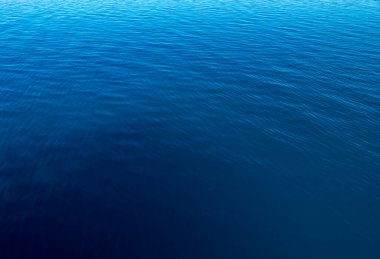 Mavi ve turuncu berrak su dokusu. Okyanusun ve denizin arkaplanı güneşle aydınlanıyor..