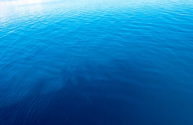 Mavi ve turuncu berrak su dokusu. Okyanusun ve denizin arkaplanı güneşle aydınlanıyor..