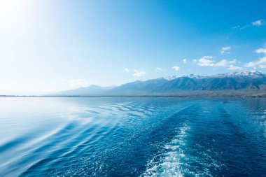 Gemideki suda ayak izleri. Mavi suda beyaz dalga. Mavi deniz suyu. Su ve gökyüzü. Gökyüzünün doğal okyanus yüzeyi. Denizde bir yaz günü manzarası.