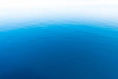 Mavi ve turuncu berrak su dokusu. Okyanusun ve denizin arkaplanı güneşle aydınlanıyor..