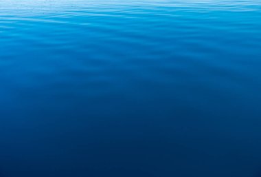 Mavi ve turuncu berrak su dokusu. Okyanusun ve denizin arkaplanı güneşle aydınlanıyor..