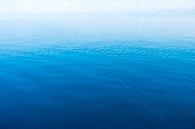 Mavi ve turuncu berrak su dokusu. Okyanusun ve denizin arkaplanı güneşle aydınlanıyor..