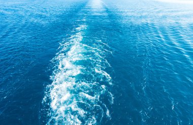 Gemideki suda ayak izleri. Mavi suda beyaz dalga. Mavi deniz suyu. Su ve gökyüzü. Gökyüzünün doğal okyanus yüzeyi. Denizde bir yaz günü manzarası.
