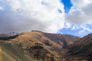 Dağlar mavi gökyüzüne ve bulutlara karşı. Dağda madencilik için bir taş ocağı var. Kırgızistan, Ak-Tuz