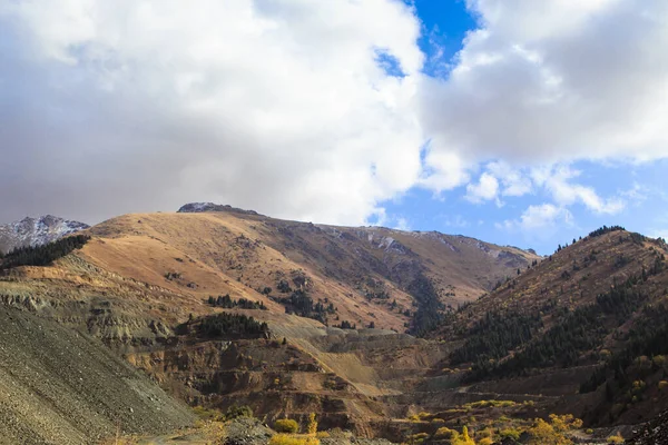 Mountains against the blue sky and clouds. On the mountain is a section of a quarry for mining. Kyrgyzstan, Ak-Tuz