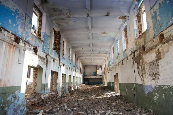 Old abandoned building. Ruins of a former factory. Dirty, dirty walls, large windows. View of mountains and trees.