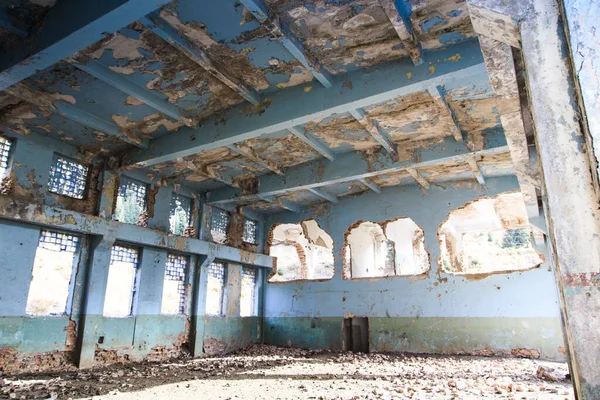 Old abandoned building. Ruins of a former factory. Dirty, dirty walls, large windows. View of mountains and trees.