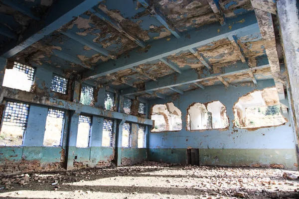 Old abandoned building. Ruins of a former factory. Dirty, dirty walls, large windows. View of mountains and trees.