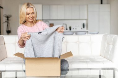 Tatmin olmuş, şık, orta yaşlı, sarışın bir kadın paket kutusunu açar ve hediye paketini açar.
