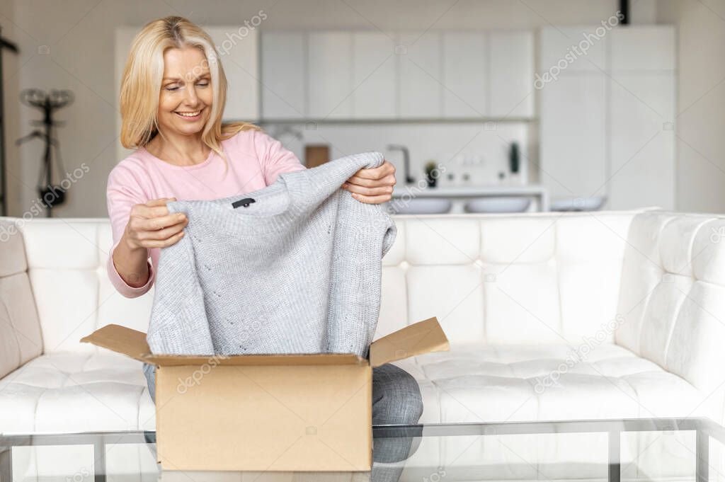 Satisfied stylish mid age blonde woman opens parcel carton box, unpacking received gift