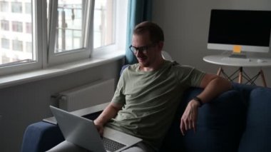 Kanepede dizüstü bilgisayarla oturan sakallı yakışıklı Avrupalı genç adam.