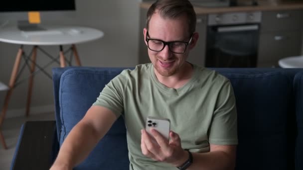 Un gars souriant portant une tenue décontractée parle par vidéo se connecter sur le smartphone — Video