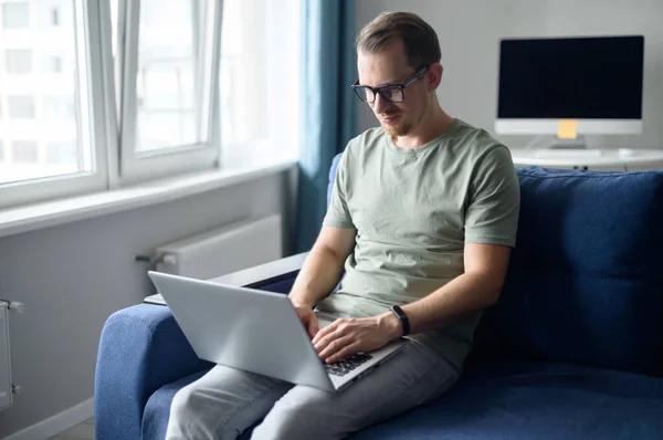Молодой бизнесмен-фрилансер сидит на диване и смотрит на ноутбук — стоковое фото