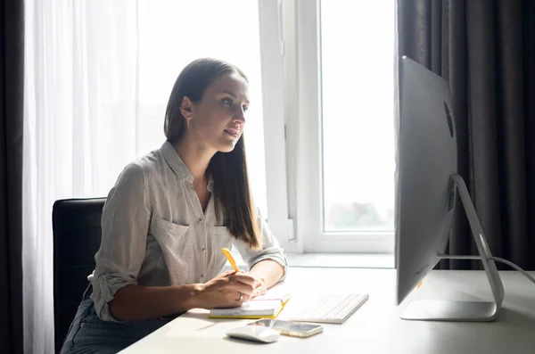 Studentin studiert von zu Hause aus, sitzt am Schreibtisch und macht sich Notizen — Stockfoto