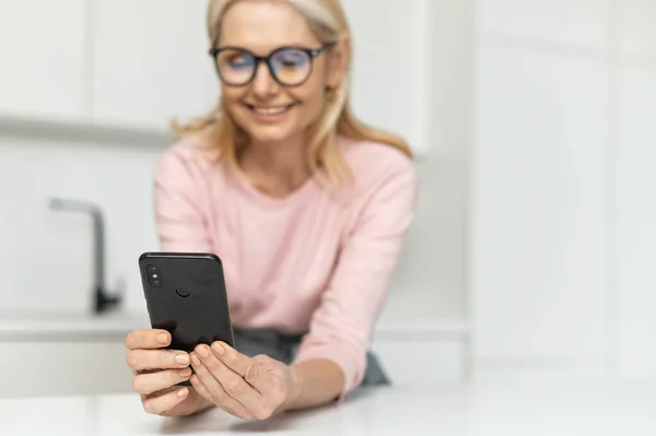 Mujer rubia feliz pasa el ocio con un teléfono inteligente en casa — Foto de Stock