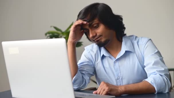 Розчарований молодий індіанець, який сидить за столом, за допомогою ноутбука. — стокове відео