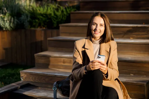 Молодая женщина печатает сообщение по телефону, сидя на улице в городе — стоковое фото