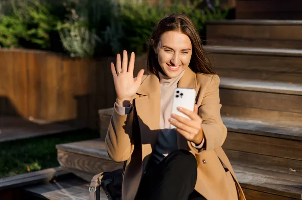 Estudante feminina sentada ao ar livre nos passos e usando smartphone para conexão de vídeo — Fotografia de Stock