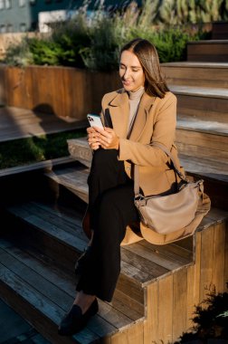 Genç bir kadın merdivenlerde oturur, akıllı telefondan sörf yapar.