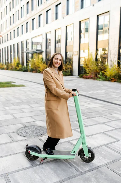 Felice donna d'affari cavalcando in smart casual abbigliamento equitazione in ufficio su un e-scooter — Foto Stock