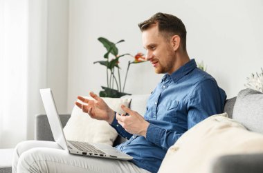 Dizüstü bilgisayarın web kamerasına bakıp konuşan genç bir adam.