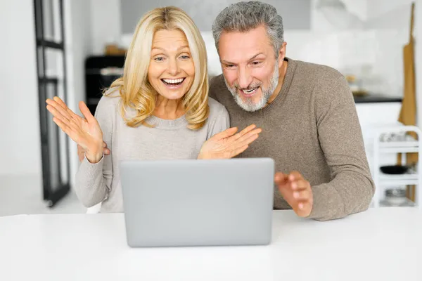 Шокована пара середнього віку дивиться на екран ноутбука, здивована несподіваними новинами — стокове фото