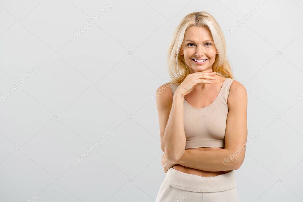 Happy carefree middle-aged lady stands in studio, isolated on grey
