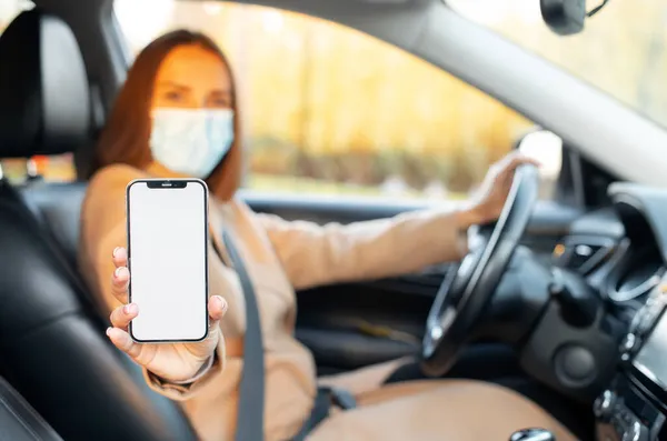 Молода жінка в хірургічній масці показує мобільний телефон з порожнім порожнім екраном — стокове фото