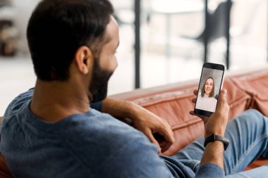 Hintli bir adam elinde akıllı telefon tutuyor ve internette genç bir kadınla konuşuyor.